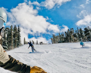 Person skiing down a snowy slope with trees and blue sky in the background